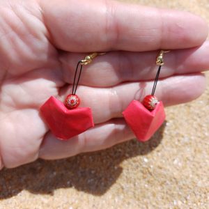 Boucles d'oreilles origami cœur rouge faites main tenues dans une main, fond sable