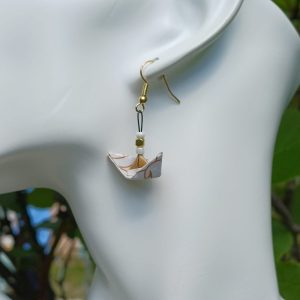 Boucles d'oreilles origami petit bateau blanc à volutes dorées portées sur mannequin bijou fond végétal