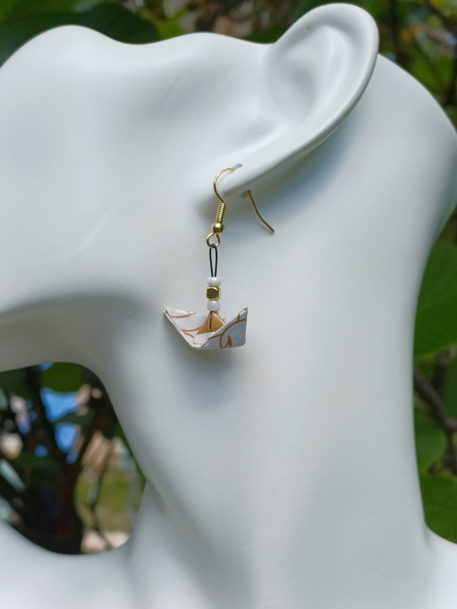 Boucles d'oreilles origami petit bateau blanc à volutes dorées portées sur mannequin bijou fond végétal