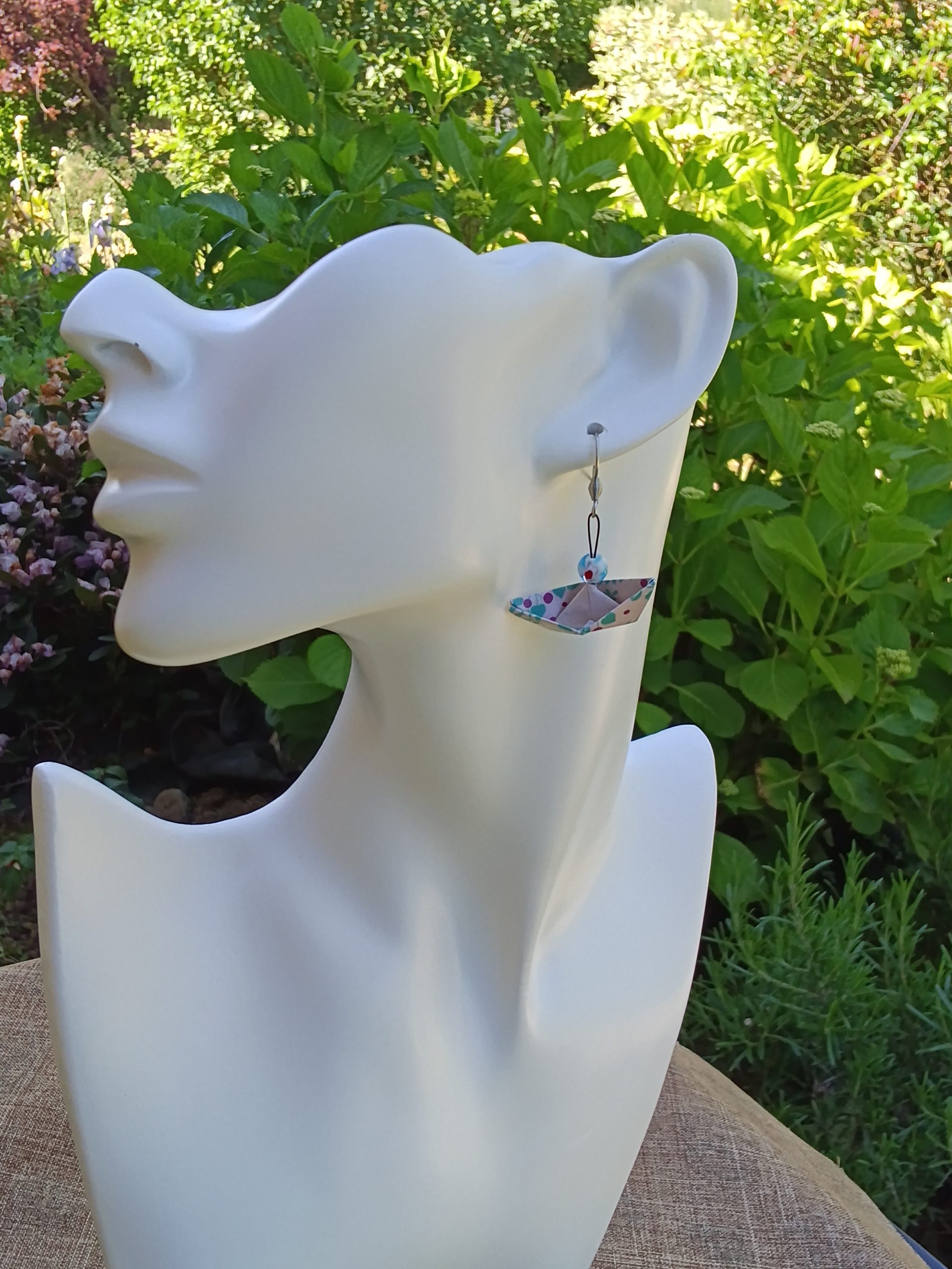 Boucles d'oreilles origami bateau blanc à motifs floraux turquoise et rose avec perle millefiori bleue, portées sur mannequin fond végétal