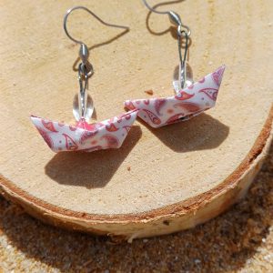 Paire de boucles d'oreilles origami bateau blanc motifs paisley rose posées sur rondelle de bois dans le sable