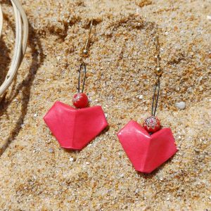 Paire de boucles d'oreilles origami en forme de cœur rouge nacré avec perles millefiori, posées sur le sable