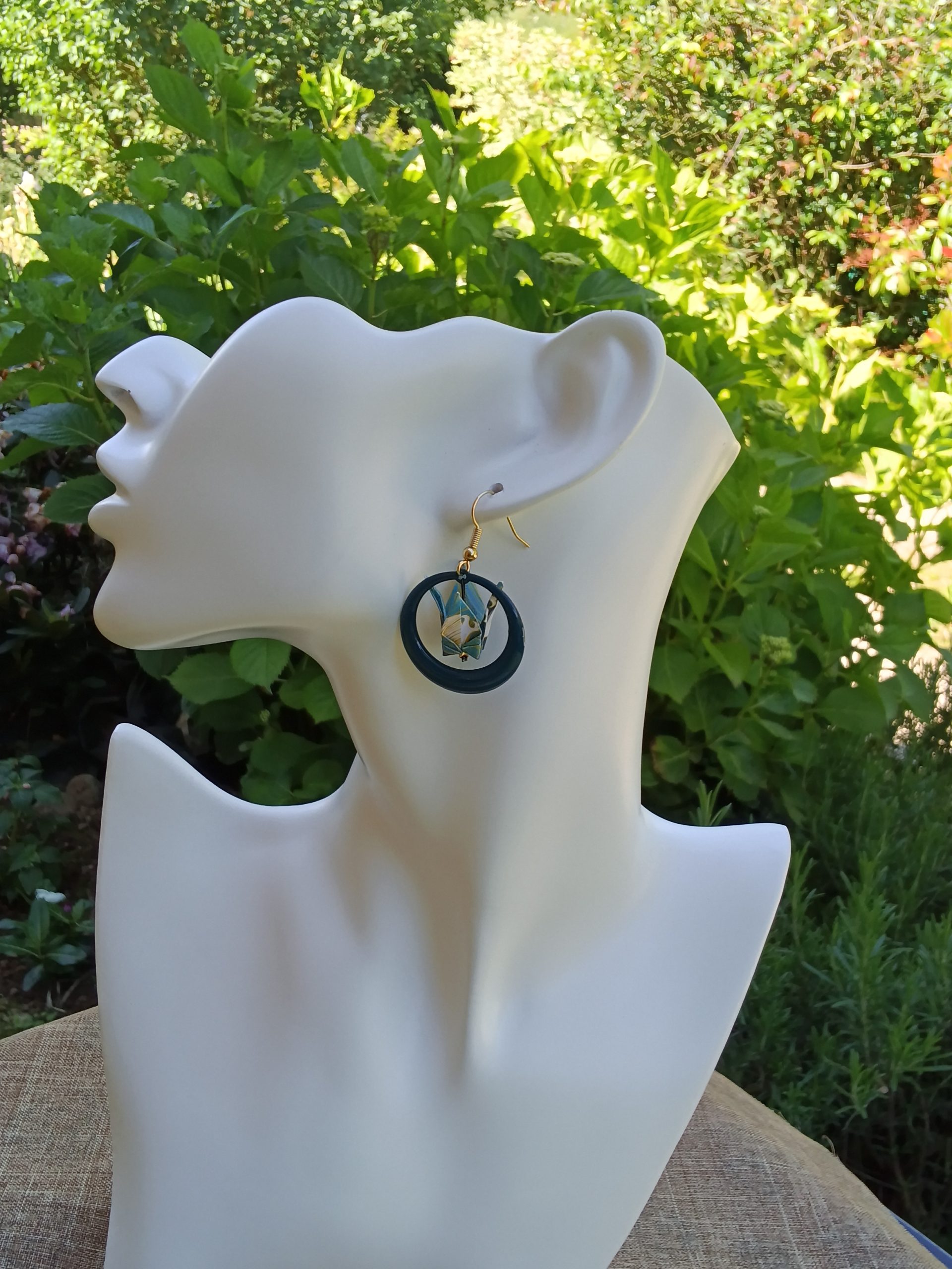 Boucles d'oreilles origami grue blanche créole résine bleu canard portées sur mannequin bijou fond jardin