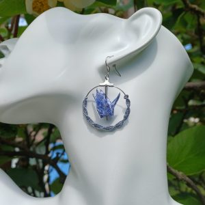 Boucles d'oreilles origami grue bleue géométrique dans créole macramé bleu ardoise, portées sur mannequin bijou fond végétal