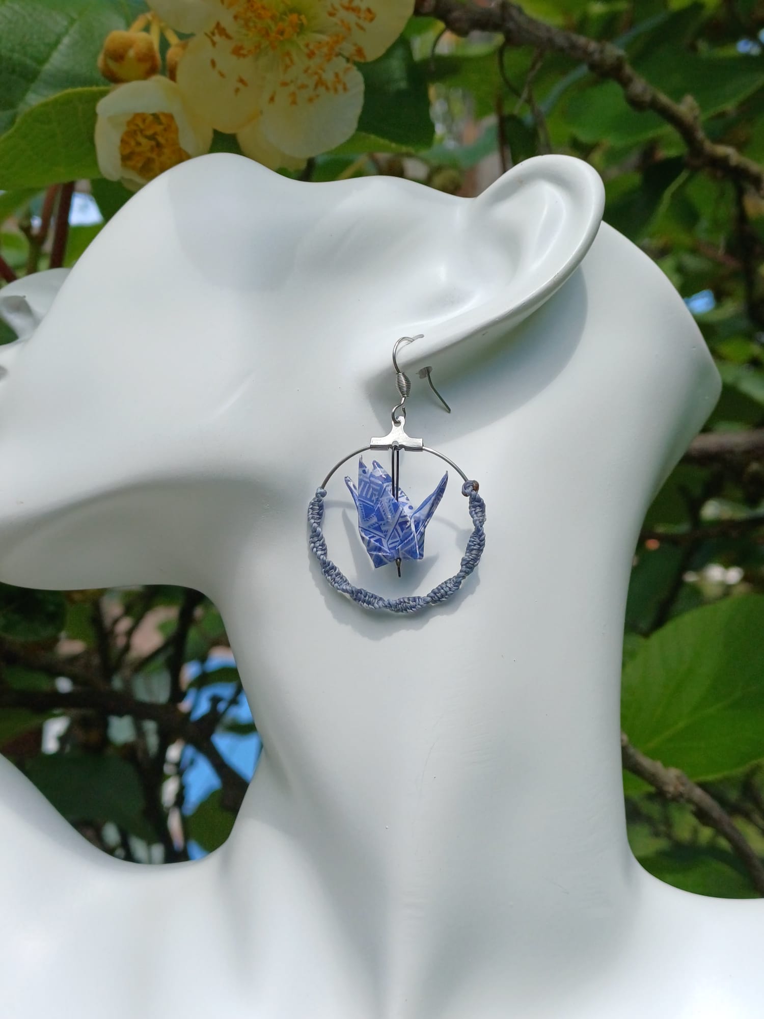 Boucles d'oreilles origami grue bleue géométrique dans créole macramé bleu ardoise, portées sur mannequin bijou fond végétal