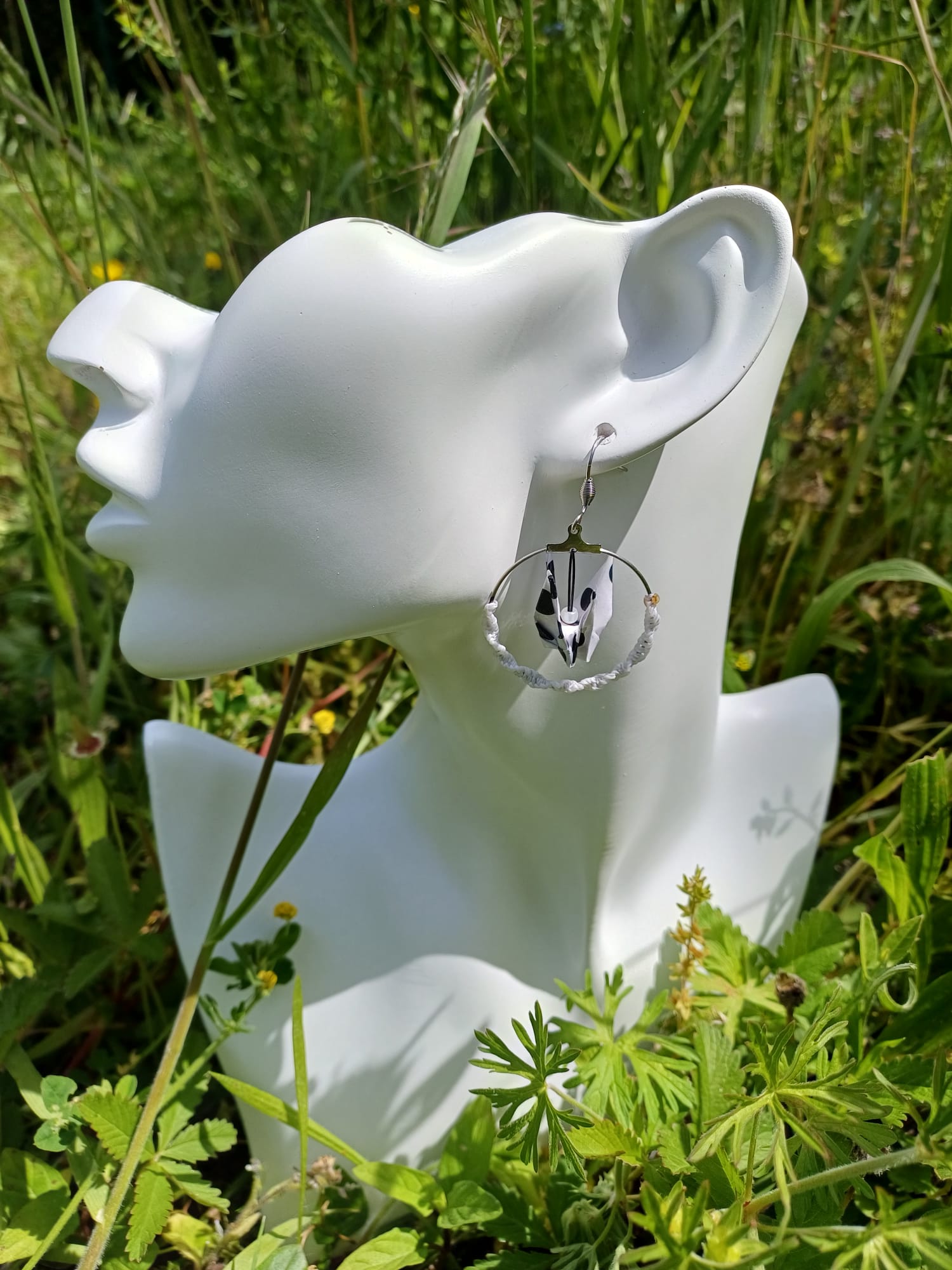 Boucles d'oreilles origami grue dalmatienne noir et blanc dans créole macramé blanc, portées sur mannequin fond prairie