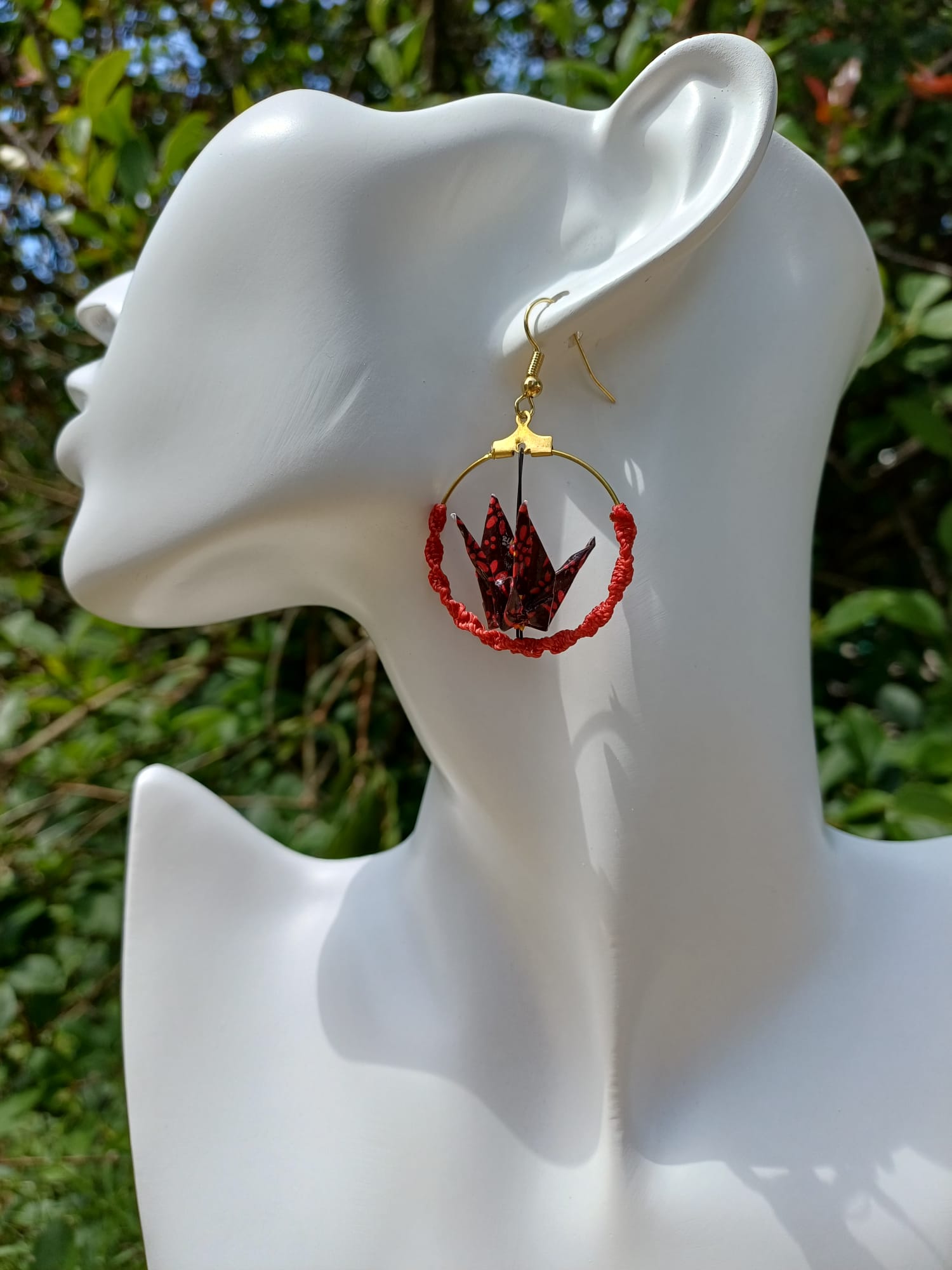 Boucles d'oreilles origami grue bordeaux dans créole macramé rouge, portées sur mannequin bijou fond végétal