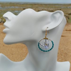 Boucle d'oreille origami grue lagon, cerceau doré et cordon turquoise tressé, portée sur mannequin bijou, fond de marais et sable
