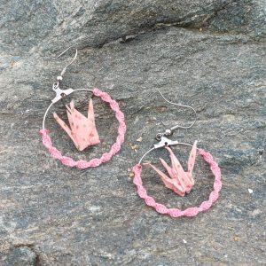 : Paire de boucles d'oreilles origami grues roses à pois dans des cerceaux tressés roses, posées sur une pierre