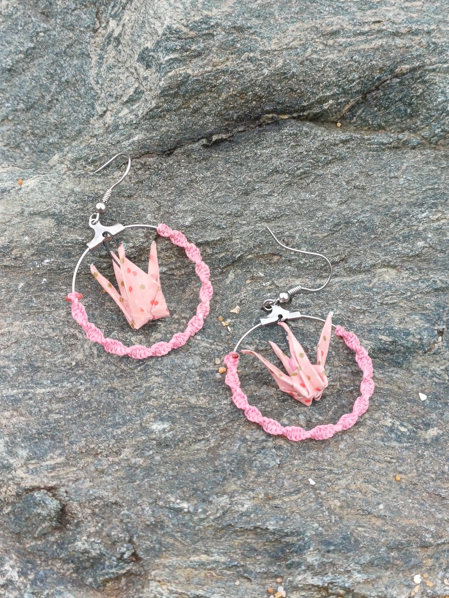 : Paire de boucles d'oreilles origami grues roses à pois dans des cerceaux tressés roses, posées sur une pierre