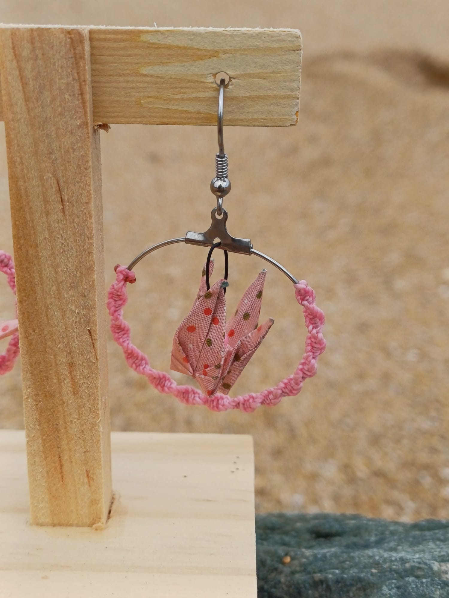 Boucle d'oreille origami en forme de grue rose à pois, cerceau enroulé de cordon rose, suspendue sur présentoir bois